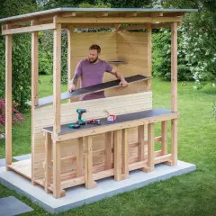 Mann baut eine Gartenbar selber. Holzkonstruktion mit Dach, Tresen und Werkzeug.