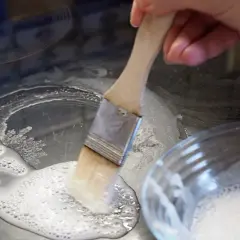 Mit einem Pinsel wird eine Paste aus Backpulver als Reinigungsmittel auf ein Ceranfeld aufgetragen, um hartnäckige Flecken zu entfernen.
