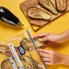 Hände legen Auberginenscheiben zum Aubergine einfrieren in einen Gefrierbeutel.