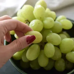 Eine Hand pflückt grüne Weintrauben aus einer Schüssel. Perfekt zum Snacken oder um sie später einzufrieren.