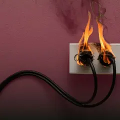 Steckdose brennt! Was tun? Zwei Kabel stecken in einer brennenden Steckdose. Rauch steigt auf. Sofort Strom abschalten!