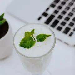 Erfrischender Drink mit Minze, ideal zum Minze einfrieren für später. Daneben eine kleine Pflanze und ein Laptop.