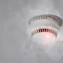 Rauchmelder mit rotem Licht und Dampf, der einen Fehlalarm durch hohe Luftfeuchtigkeit auslöst.