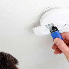 Ein Mann wechselt die Batterie eines Rauchmelders. Das Piepen bei leerer Batterie ist ein wichtiges Warnsignal.