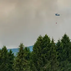 Helikopter bekämpft Waldbrand. Giftiger Rauch steigt auf, der Geruch nach Brand liegt in der Luft.