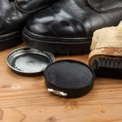Schwarze Schuhe, Schuhcreme und Bürste auf Holz. So lassen sich Schuhcremeflecken entfernen und die Schuhe pflegen.