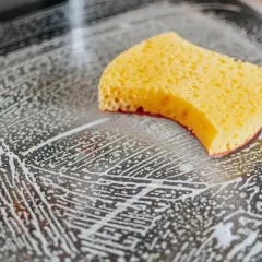 Gelber Schwamm auf schmutziger Oberfläche mit Rasierschaum. Kragenschmutz entfernen mit Schaum ist einfach.