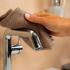Eine Hand reinigt mit einem braunen Tuch eine glänzende Armatur.