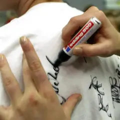 Eine Hand schreibt mit einem Edding-Filzstift Autogramme auf ein weißes T-Shirt. Tipps für hausmittel filzstift entfernen sind hier nicht zu sehen.