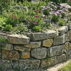 Eine stabile Trockenmauer mit bunten Blumen und grünen Pflanzen, die sich harmonisch in den Garten einfügt.