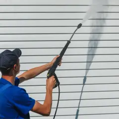 Mann mit Kappe reinigt mit Hochdruckreiniger die weiße Fassade. Fassade reinigen selber machen ist einfach!