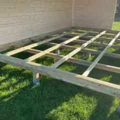 Das Fundament für das Gartenhaus bauen: Holzbalken auf Stelzlagern im Gras, bereit für den Boden.