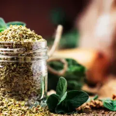 Ein Glas mit getrocknetem Oregano, daneben frische Zweige. Perfekt für die Küche, um Speisen zu würzen.