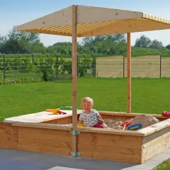 Ein Kind spielt im **Sandkasten selber bauen**. Der Holzsandkasten mit Sonnendach steht im Garten.