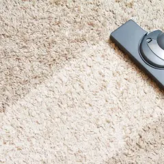 Ein Staubsaugerkopf reinigt einen hellbeigen Hochflorteppich. Tipps zur auslegware reinigen mit hausmitteln.