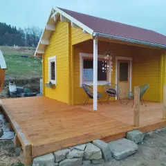 Ein gelber Holzschuppen mit Terrasse, ideal zum schuppen selber bauen. Daneben eine Holzfasssauna.