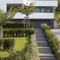 Moderner Garten am Hang mit gepflasterter Auffahrt, Treppen und üppiger Bepflanzung.