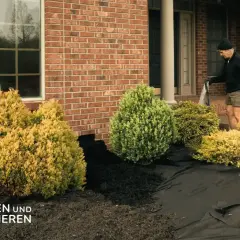 Mann legt Vlies aus, um den Vorgarten zu gestalten. Neue Pflanzen und Mulch werden vorbereitet.