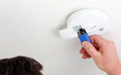 Ein Mann wechselt die Batterie eines Rauchmelders. Das Piepen bei leerer Batterie ist ein wichtiges Warnsignal.