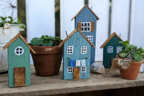 Kleine Holzhäuser, die zum **Holz Gartendeko selber machen** einladen. Bunte Häuschen mit Wäscheleine und Blumentöpfen.
