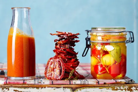 Glas mit eingelegten Tomaten, getrocknete Tomaten und eine Flasche Tomatensauce – alles für Tomaten haltbar machen.