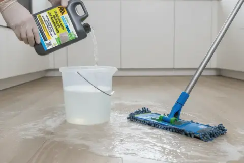 Reinigungsmittel wird in Eimer gegossen, um flecken auf steinfliesen zu entfernen. Ein Mopp liegt bereit.
