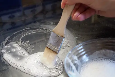 Mit einem Pinsel wird eine Paste aus Backpulver als Reinigungsmittel auf ein Ceranfeld aufgetragen, um hartnäckige Flecken zu entfernen.