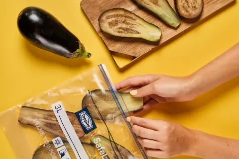 Hände legen Auberginenscheiben zum Aubergine einfrieren in einen Gefrierbeutel.