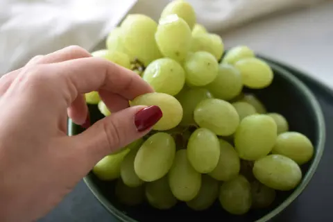 Eine Hand pflückt grüne Weintrauben aus einer Schüssel. Perfekt zum Snacken oder um sie später einzufrieren.