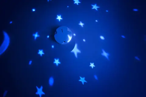 Ein weißer Rauchmelder projiziert Sterne und einen Mond an eine blaue Wand.