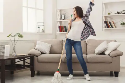 Frau singt und tanzt mit einem Mopp, während sie ihr Linoleum mit Hausmitteln reinigt.