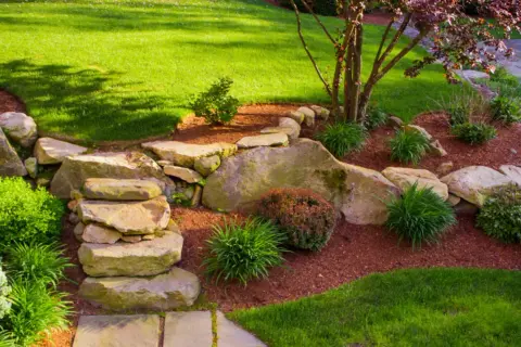 Ein schöner Garten gestalten mit wenig Geld: Steine, Rindenmulch und pflegeleichte Pflanzen schaffen eine natürliche Optik.