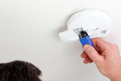 Ein Mann wechselt die Batterie eines Rauchmelders. Das Piepen bei leerer Batterie ist ein wichtiges Warnsignal.