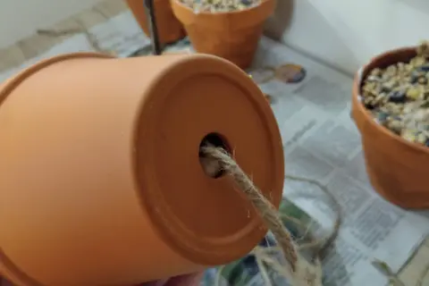 Ein Blumentopf wird zur Vogelfutterstation. Ein Seil wird durch das Loch gezogen, um die Futterstation aufzuhängen.