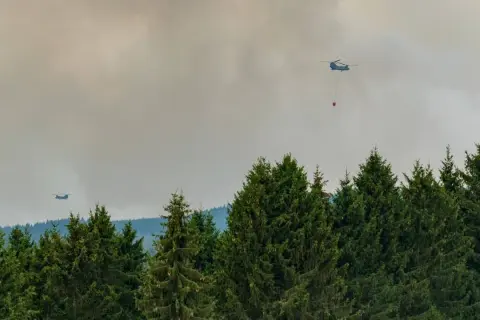 Helikopter bekämpft Waldbrand. Giftiger Rauch steigt auf, der Geruch nach Brand liegt in der Luft.