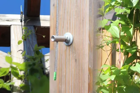 Selbstgebaute Rankhilfe aus Metall: Ein Drahtseil wird an einem Holzpfosten befestigt, um Kletterpflanzen Halt zu geben.