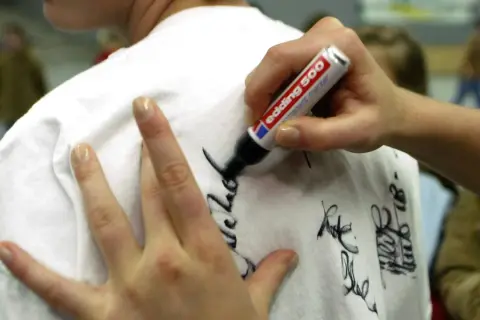 Eine Hand schreibt mit einem Edding-Filzstift Autogramme auf ein weißes T-Shirt. Tipps für hausmittel filzstift entfernen sind hier nicht zu sehen.