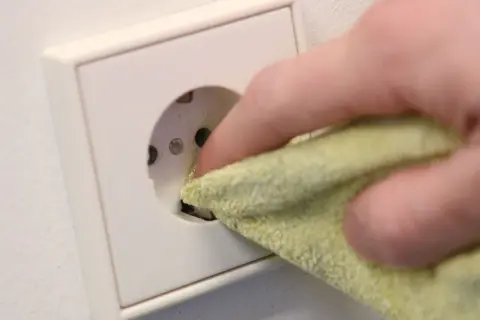 Finger mit Tuch reinigt Steckdose, um sie sicher und sauber zu halten. Steckdosen reinigen ohne abschrauben ist so einfach.
