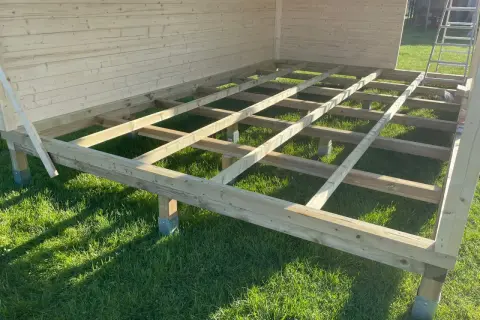 Das Fundament für das Gartenhaus bauen: Holzbalken auf Stelzlagern im Gras, bereit für den Boden.