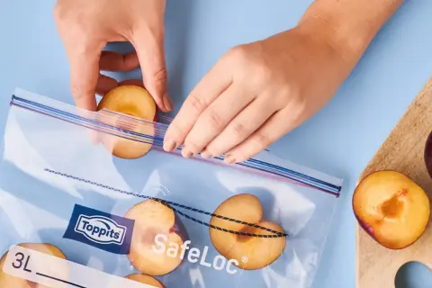 Hände legen halbe Pflaumen in einen Gefrierbeutel. So lassen sich die Früchte perfekt für später einfrieren.