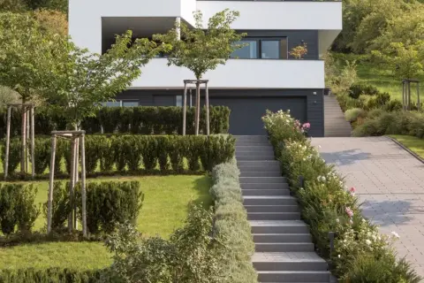 Moderner Garten am Hang mit gepflasterter Auffahrt, Treppen und üppiger Bepflanzung.