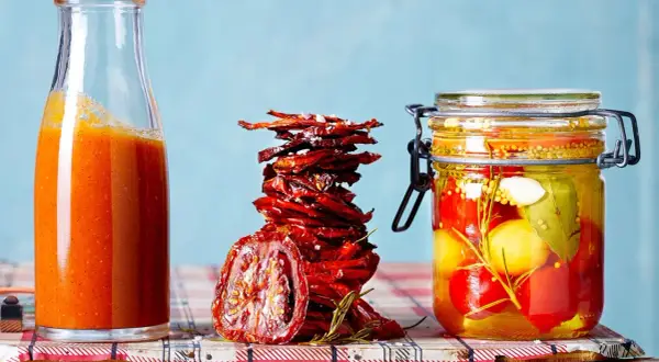 Glas mit eingelegten Tomaten, getrocknete Tomaten und eine Flasche Tomatensauce – alles für Tomaten haltbar machen.