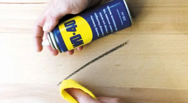 WD-40 Dose sprüht auf einen dunklen Streifen auf hellem Linoleum, der mit einem gelben Tuch abgewischt wird. So lassen sich Streifen auf Linoleum entfernen.