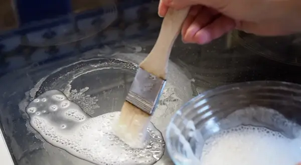 Mit einem Pinsel wird eine Paste aus Backpulver als Reinigungsmittel auf ein Ceranfeld aufgetragen, um hartnäckige Flecken zu entfernen.