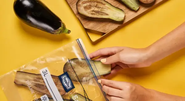 Hände legen Auberginenscheiben zum Aubergine einfrieren in einen Gefrierbeutel.
