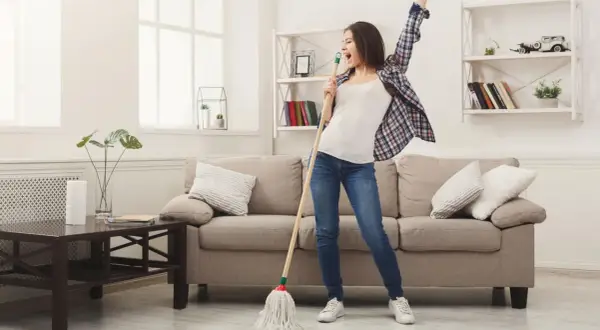 Frau singt und tanzt mit einem Mopp, während sie ihr Linoleum mit Hausmitteln reinigt.