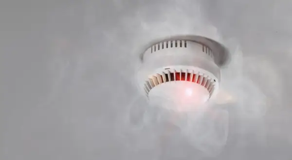 Rauchmelder mit rotem Licht und Dampf, der einen Fehlalarm durch hohe Luftfeuchtigkeit auslöst.