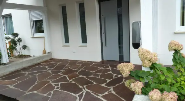 Vor dem Haus liegt ein Boden aus unregelmäßigen Porphyrplatten. Mit Hausmitteln lässt sich dieser Porphyr reinigen und erstrahlt wieder in neuem Glanz.