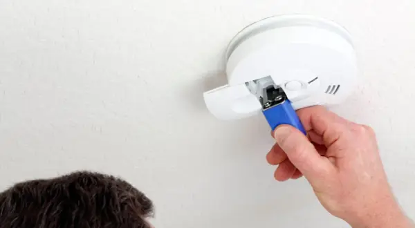 Ein Mann wechselt die Batterie eines Rauchmelders. Das Piepen bei leerer Batterie ist ein wichtiges Warnsignal.