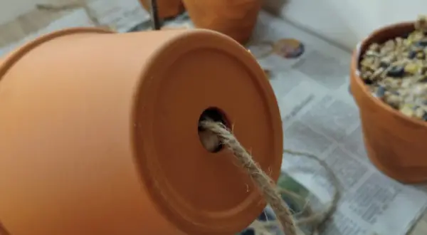 Ein Blumentopf wird zur Vogelfutterstation. Ein Seil wird durch das Loch gezogen, um die Futterstation aufzuhängen.